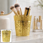 A gold ornate plastic desk organizer filled with makeup brushes on a bathroom counter.