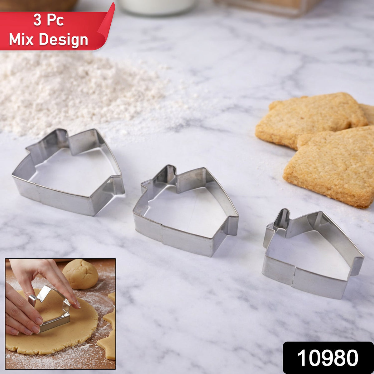 Three stainless steel house-shaped cookie cutters of varying sizes arranged on a white marble surface next to flour and