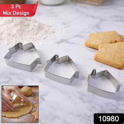 Three stainless steel house-shaped cookie cutters of varying sizes arranged on a white marble surface next to flour and