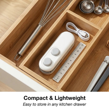 The white and grey bag sealer and cutter, a ruler, and a whisk are neatly organized in a wooden kitchen drawer.