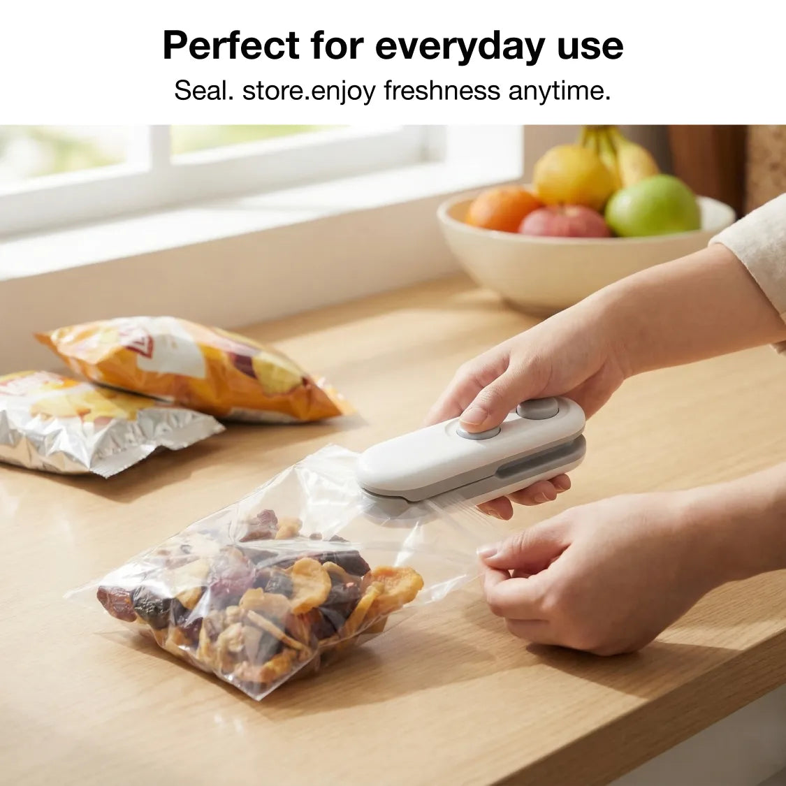 A person uses the white and grey bag sealer to seal a clear bag of dried fruit on a wooden counter.