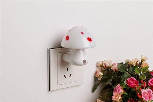 A white mushroom-shaped night light with red spots is plugged into a white wall socket next to a bouquet of flowers.