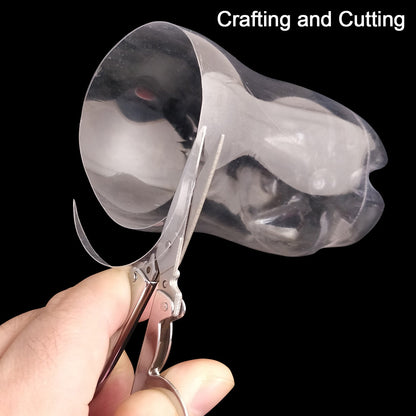 A hand uses open silver folding scissors to cut a clear plastic bottle against a black background.
