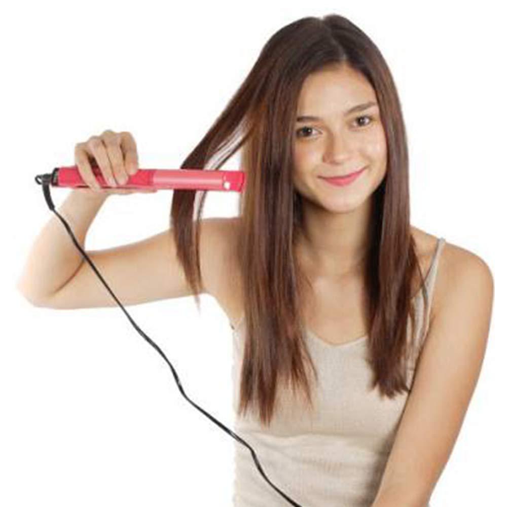 A woman with long brown hair smiles while using a pink hair straightener on a section of her hair.