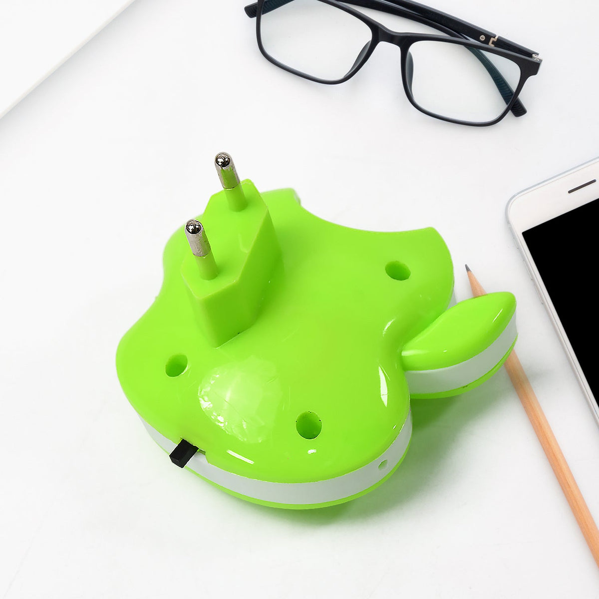 The back of the green apple-shaped LED night light with its two-pronged plug, next to glasses and a phone.