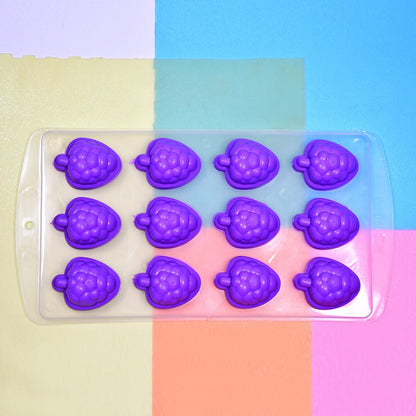 Purple silicone fruit-shaped ice cube tray on a colorful background of blue, pink, and yellow squares.