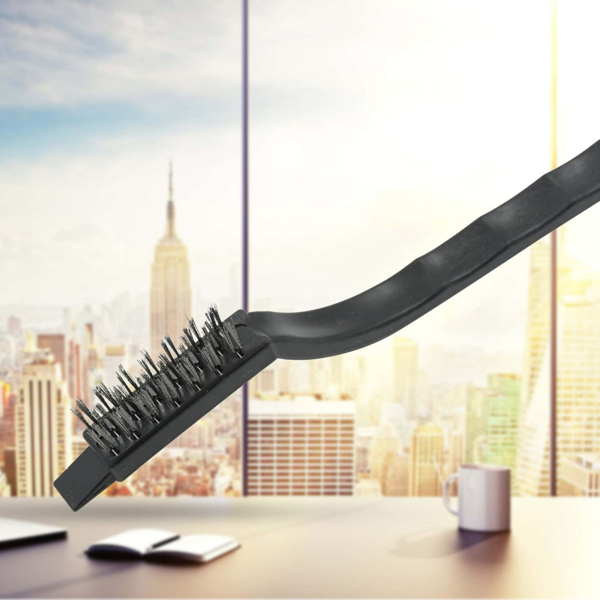 A single black-handled mini wire brush with steel bristles against a blurred city skyline background.