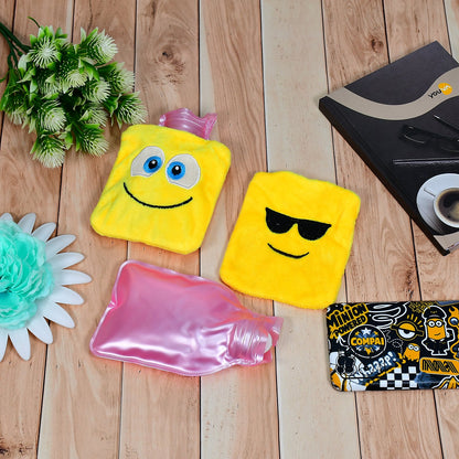 Two yellow emoji hot water bags and one pink plastic hot water bottle are on a light wood surface.