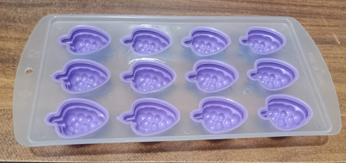 An empty purple silicone fruit-shaped ice cube tray with twelve molds, viewed from above on a wooden surface.
