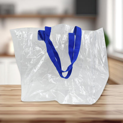 An empty clear PVC tote bag with blue handles sits on a wooden counter in a blurred kitchen background.