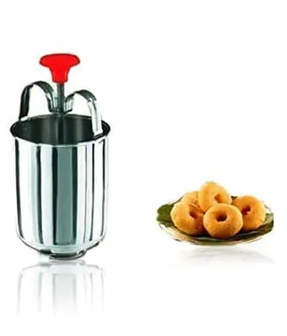 A stainless steel medu vada maker with a red handle, next to a plate of vadas on a green leaf, on a white background.