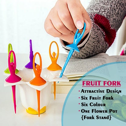 A hand placing a blue dancing doll fruit fork into a white flower-shaped stand with other colorful forks.