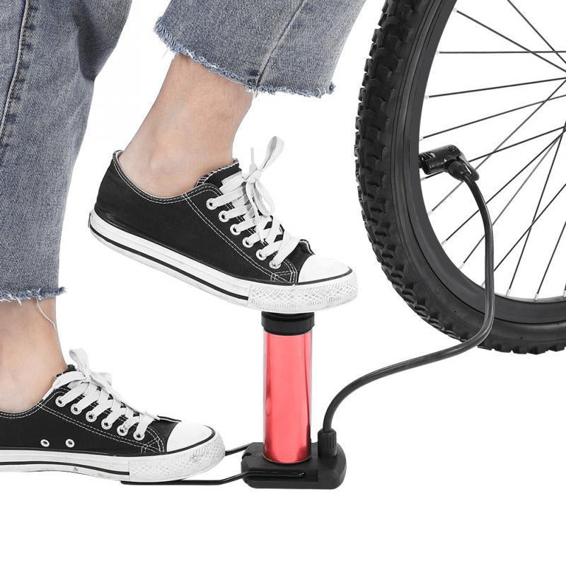 Person's feet operating a red mini foot pump to inflate a bicycle tire.