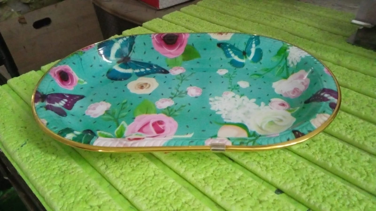 The oval turquoise tray with floral and butterfly print is placed on a textured green surface.