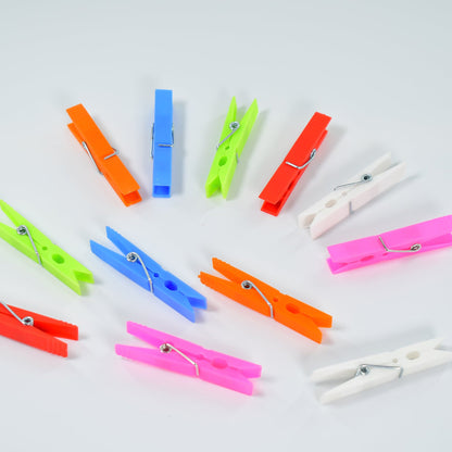 Twelve colorful plastic clothes clips scattered on a white surface, showing various colors and their metal springs.