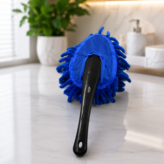 Blue microfiber duster with a black handle resting on a white marble countertop next to a green plant.