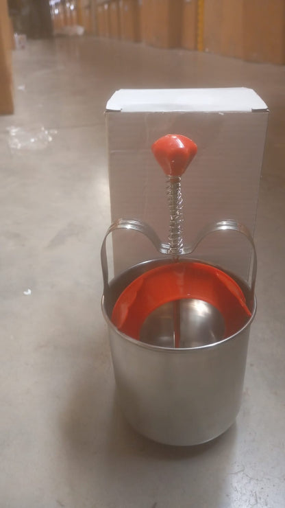 A stainless steel medu vada maker with a red handle and orange interior, in front of a white box on a concrete floor.