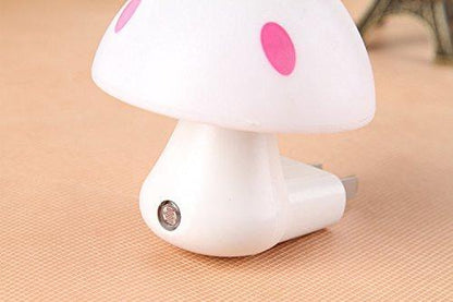 A close-up of a white mushroom-shaped night light with pink spots, showing the light sensor and plug on a textured surface.