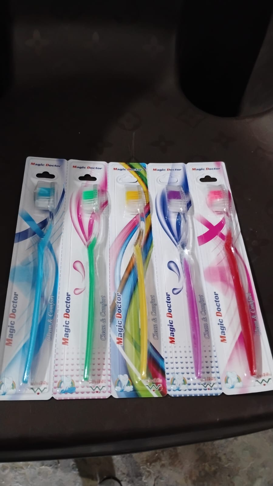 Five individually packaged 'Magic Doctor' toothbrushes with colorful designs are lined up on a dark surface.