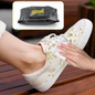 A hand uses a white wet wipe to clean yellow splatters off a beige canvas shoe on a wooden bench.