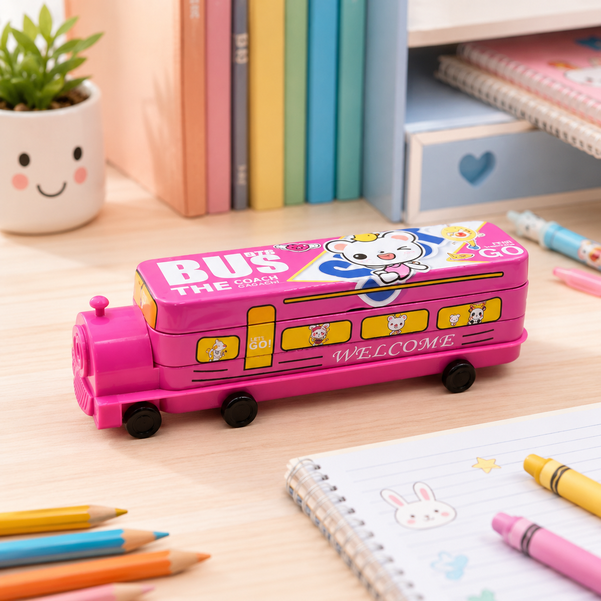 Pink bus pencil case with cartoon bear on top, surrounded by colorful stationery on a wooden desk.