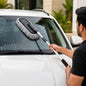A person cleaning a white car's windshield with a gray and black microfiber duster with an extendable handle.