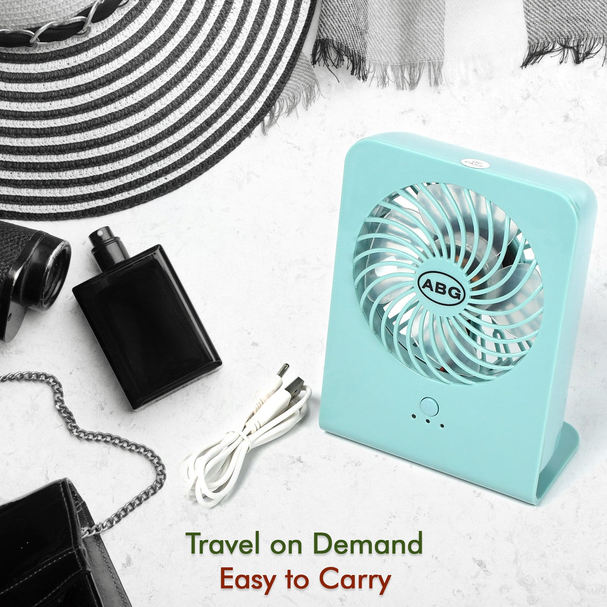 A mint green portable desk fan with a white USB cable, next to a black perfume bottle and a striped hat.