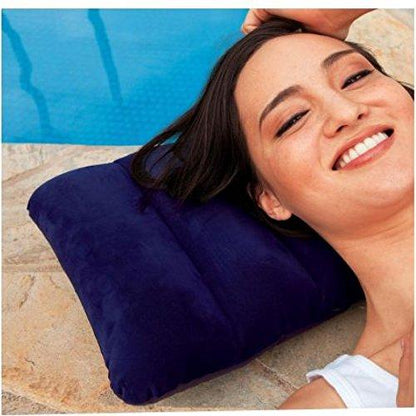 A smiling woman with dark hair rests her head on a blue velvet inflatable pillow next to a swimming pool.