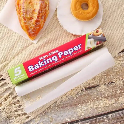 A roll of white non-stick baking paper and its red and green box on a textured fabric surface, with a pastry and a donut in