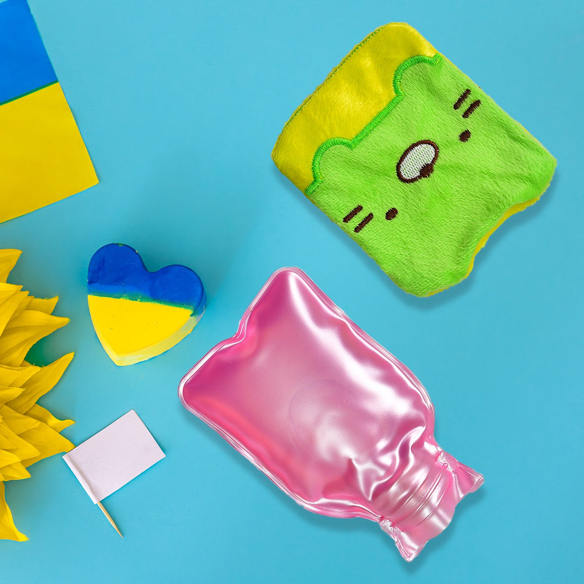 A green and yellow kitty hot water bag, pink hot water bottle, and Ukrainian flag items on a blue background.