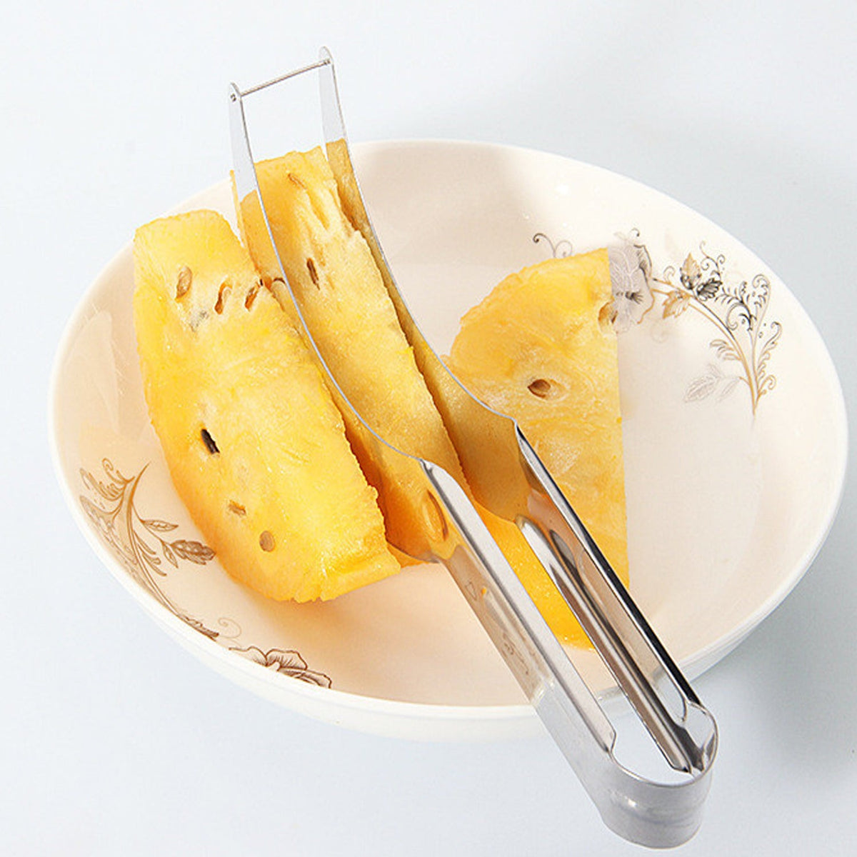 A silver stainless steel slicer holds three slices of yellow watermelon in a white bowl with a floral pattern.