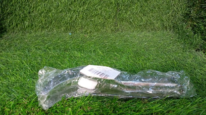 A clear plastic-wrapped stainless steel watermelon slicer with a white label lies on a vibrant green grassy surface.