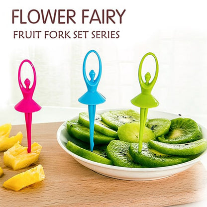 Three colorful dancing doll fruit forks, pink, blue, and green, on a wooden board with sliced kiwi and pineapple.