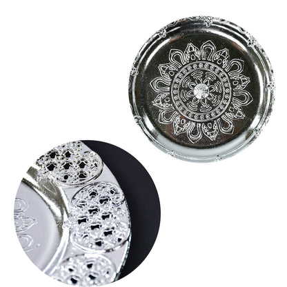 A close-up of the silver-colored plastic pooja thali's embossed center and a magnified view of its intricate filigree border.