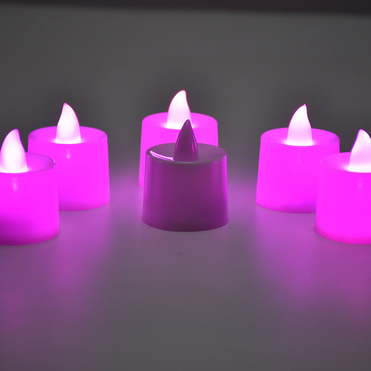 Six pink LED flameless tealights glowing on a light surface in a dimly lit room.