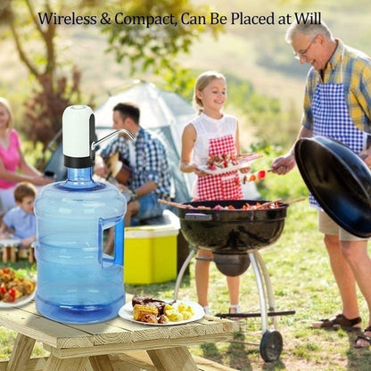 Automatic water pump on a large blue bottle on a wooden picnic table, with people barbecuing in the background.