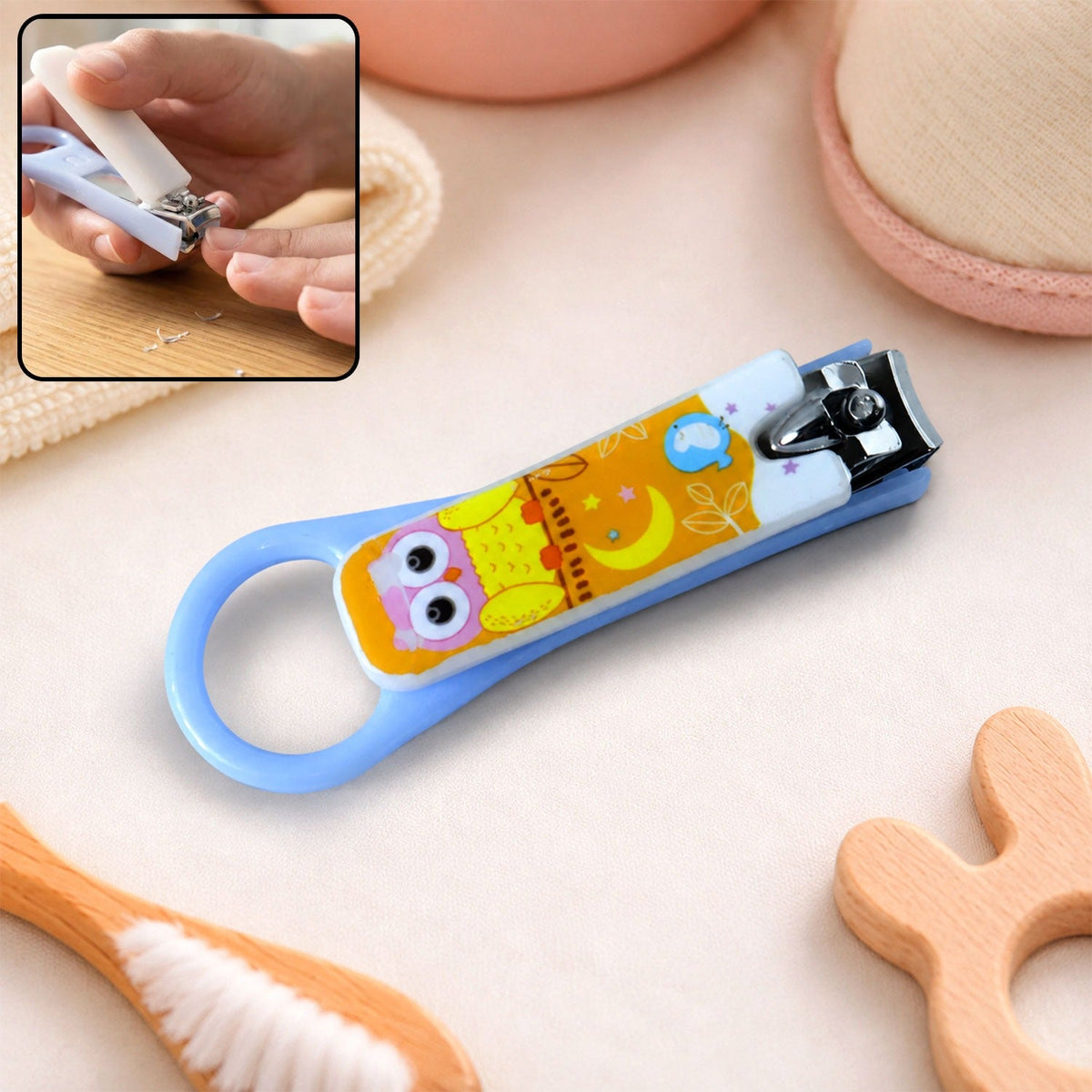 A light blue baby nail clipper with a yellow and white owl design, shown with an inset of it being used.