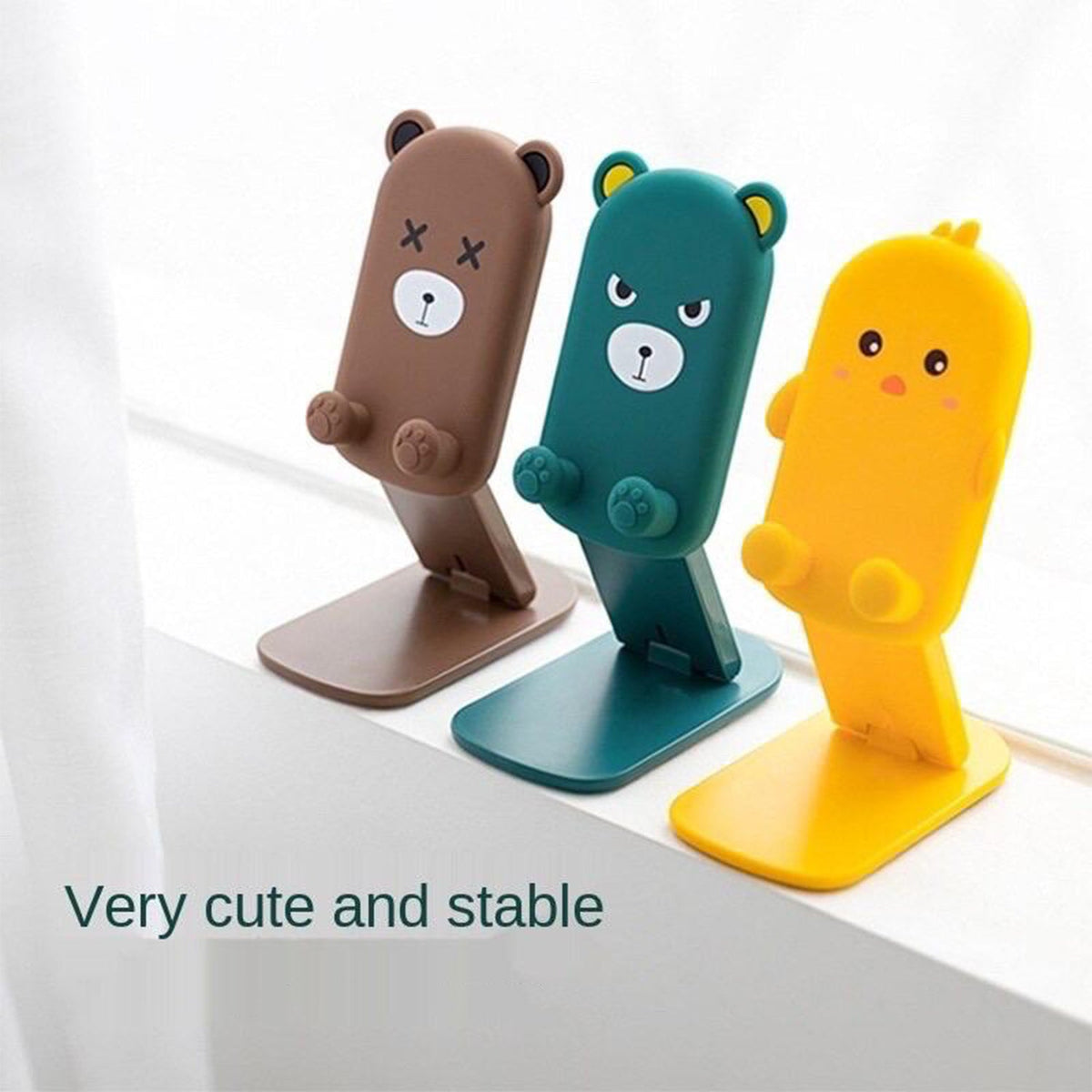 Three cartoon phone stands, brown bear, green bear, and yellow duck, are lined up on a windowsill.