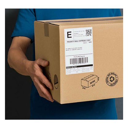A person in a blue shirt holds a brown cardboard box with a large white shipping label affixed to its side.