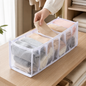 A hand places a folded beige garment into one section of a white mesh organizer filled with various clothes on a wooden