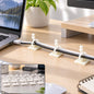 White self-adhesive clips securing black and white cables to a light wooden desk next to a laptop.