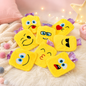 Seven yellow emoji hot water bags with various facial expressions are scattered on a white fluffy rug.
