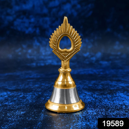 A small brass and steel pooja bell with a peacock feather design stands against a textured dark blue background.