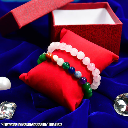 Two beaded bracelets, one pink and one multi-colored, displayed on a red velvet pillow on a blue cloth with decorative gems.