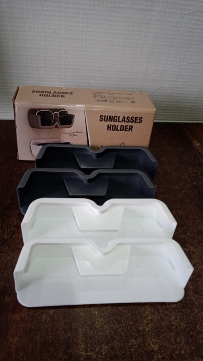 Two black and two white glasses holders stacked on a wooden surface, with two brown boxes in the background.