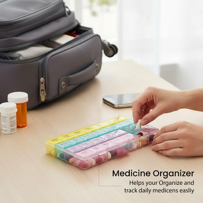 Hands place pills into the rainbow-colored organizer on a wooden table, with a travel bag in the background.
