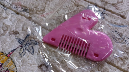 A pink heart-shaped hair thinning razor comb is sealed in clear plastic packaging on a patterned blanket.