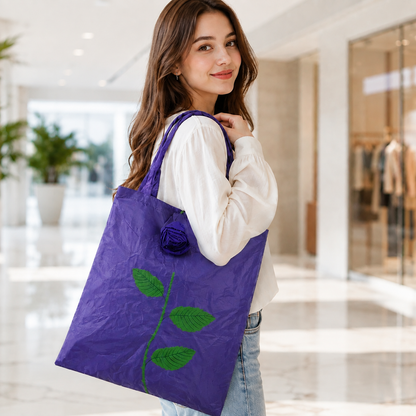 A woman carries a purple foldable shopping bag with a green leaf and rose design on her shoulder.