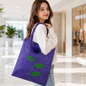 A woman carries a purple foldable shopping bag with a green leaf and rose design on her shoulder.