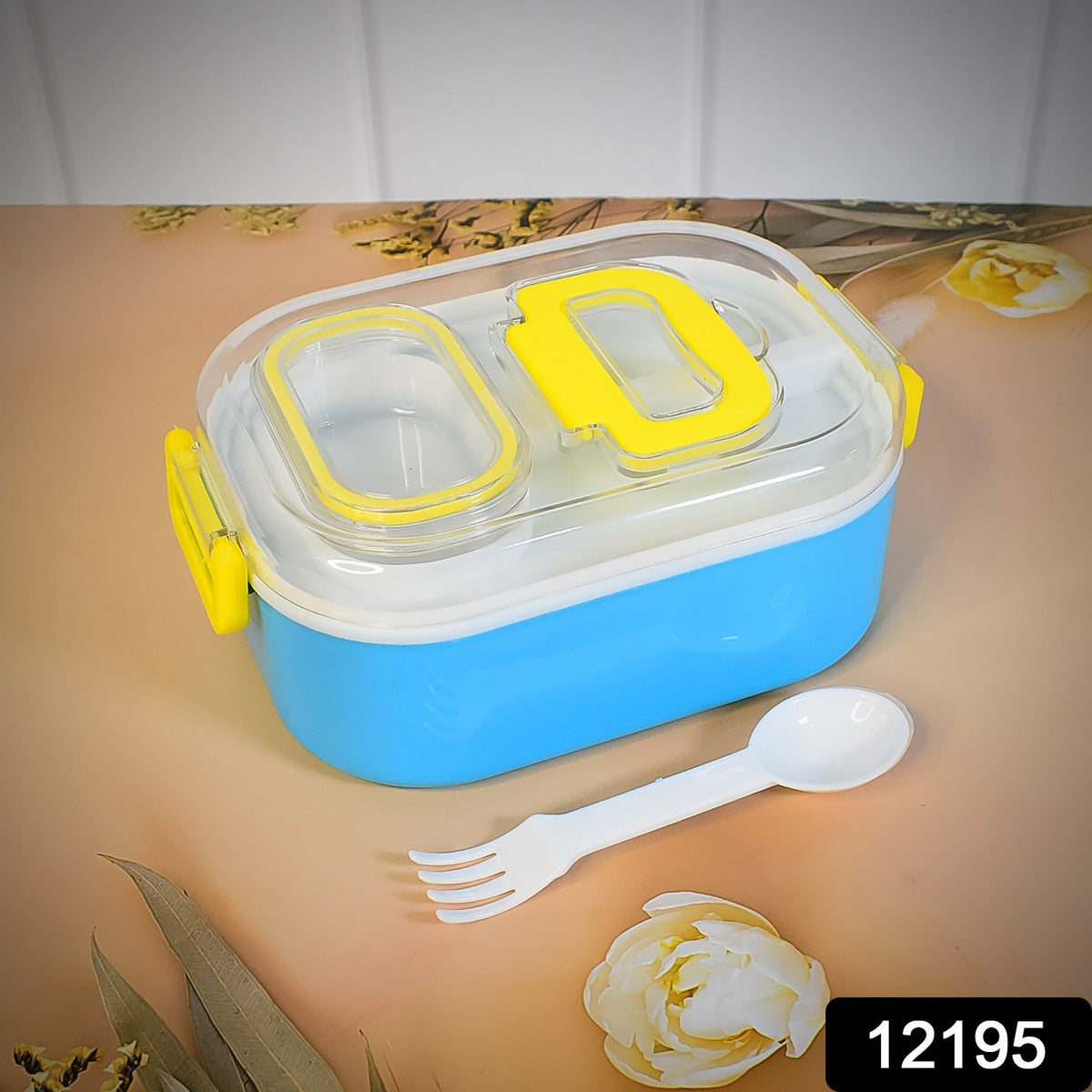 A closed blue and white lunch box with yellow accents sits on a beige surface with a white spoon-fork.